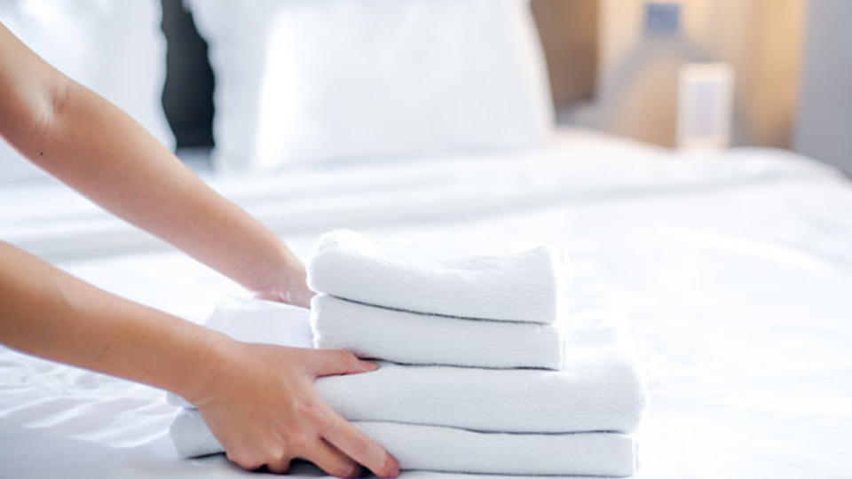 A person is holding some folded towels on top of the bed