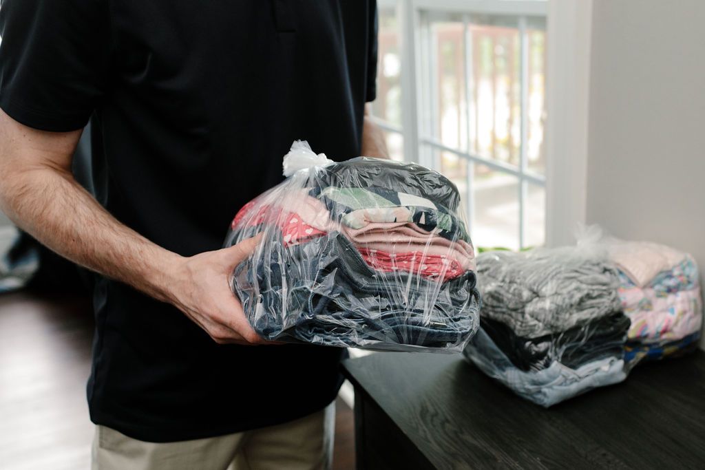 A man holding a bag of clothes in plastic.