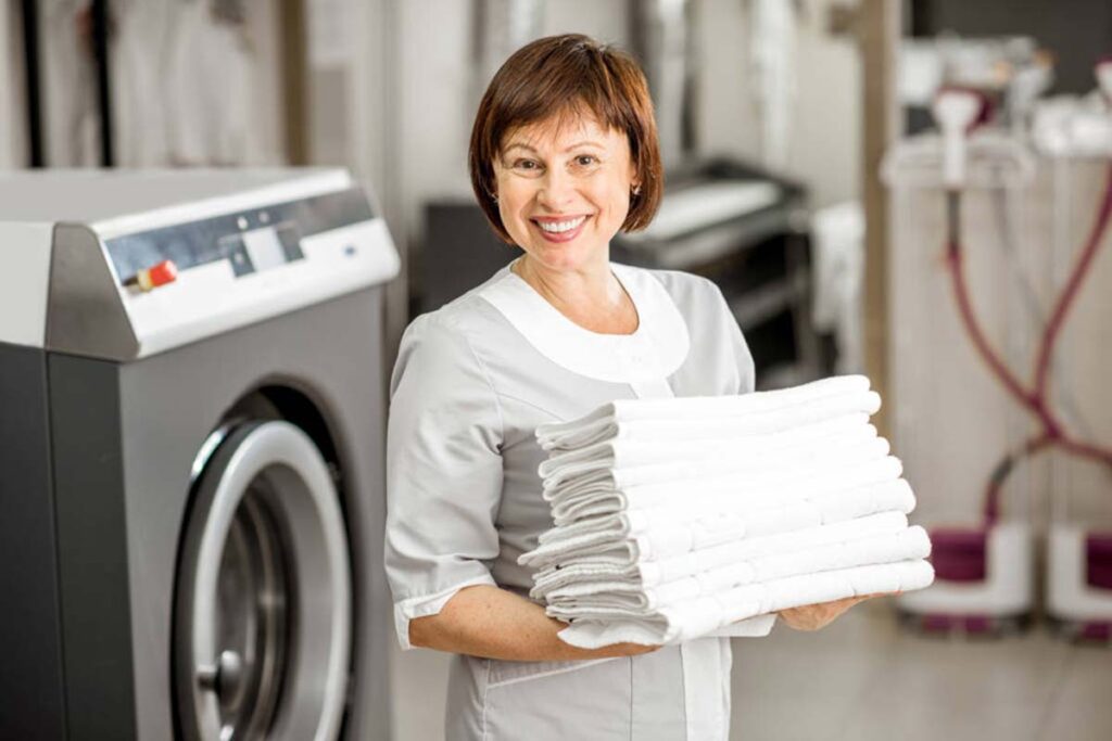 A woman holding some folded towels in front of a washing machine